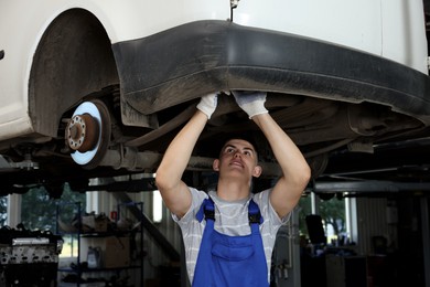 Photo of Young auto mechanic fixing lifted car at automobile repair shop