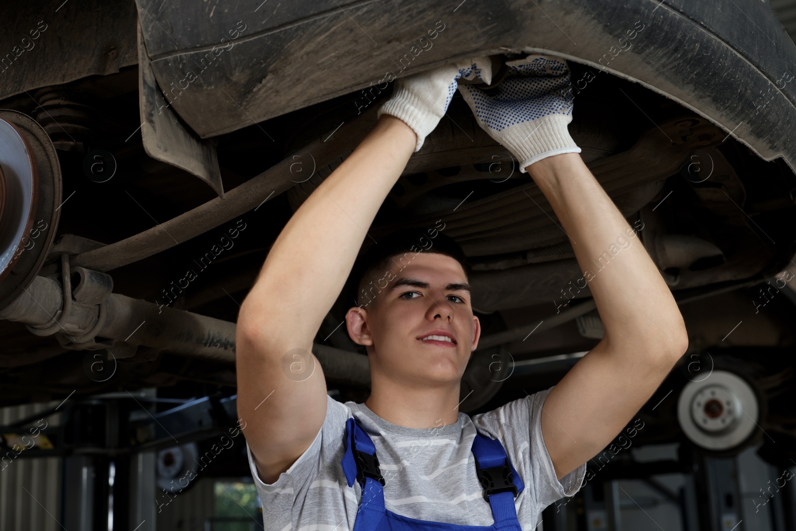 Photo of Young auto mechanic fixing lifted car at automobile repair shop