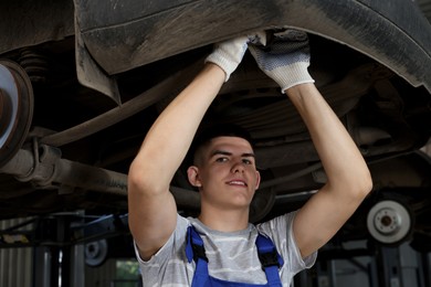 Young auto mechanic fixing lifted car at automobile repair shop