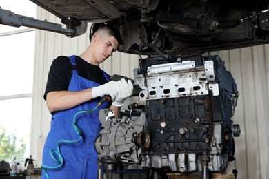 Photo of Young auto mechanic fixing motor at automobile repair shop, low angle view. Car diagnostic