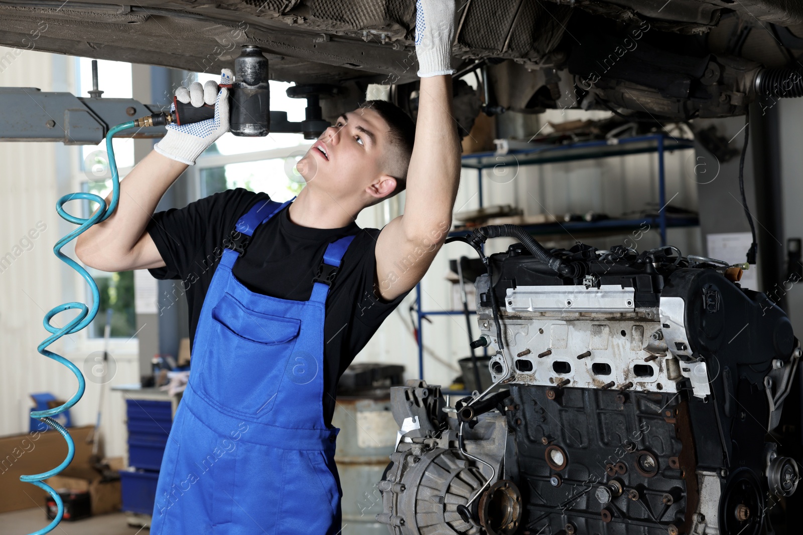 Photo of Young auto mechanic fixing lifted car at automobile repair shop