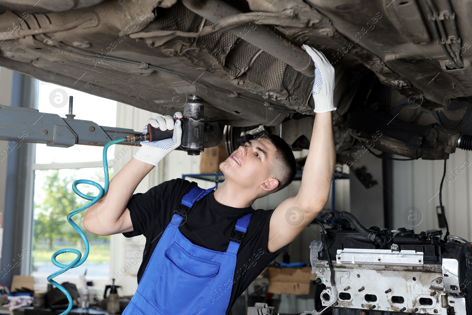 Photo of Young auto mechanic fixing lifted car at automobile repair shop