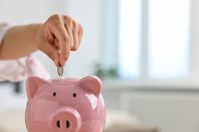 Photo of Woman putting coin into pink piggy bank at home, closeup. Space for text