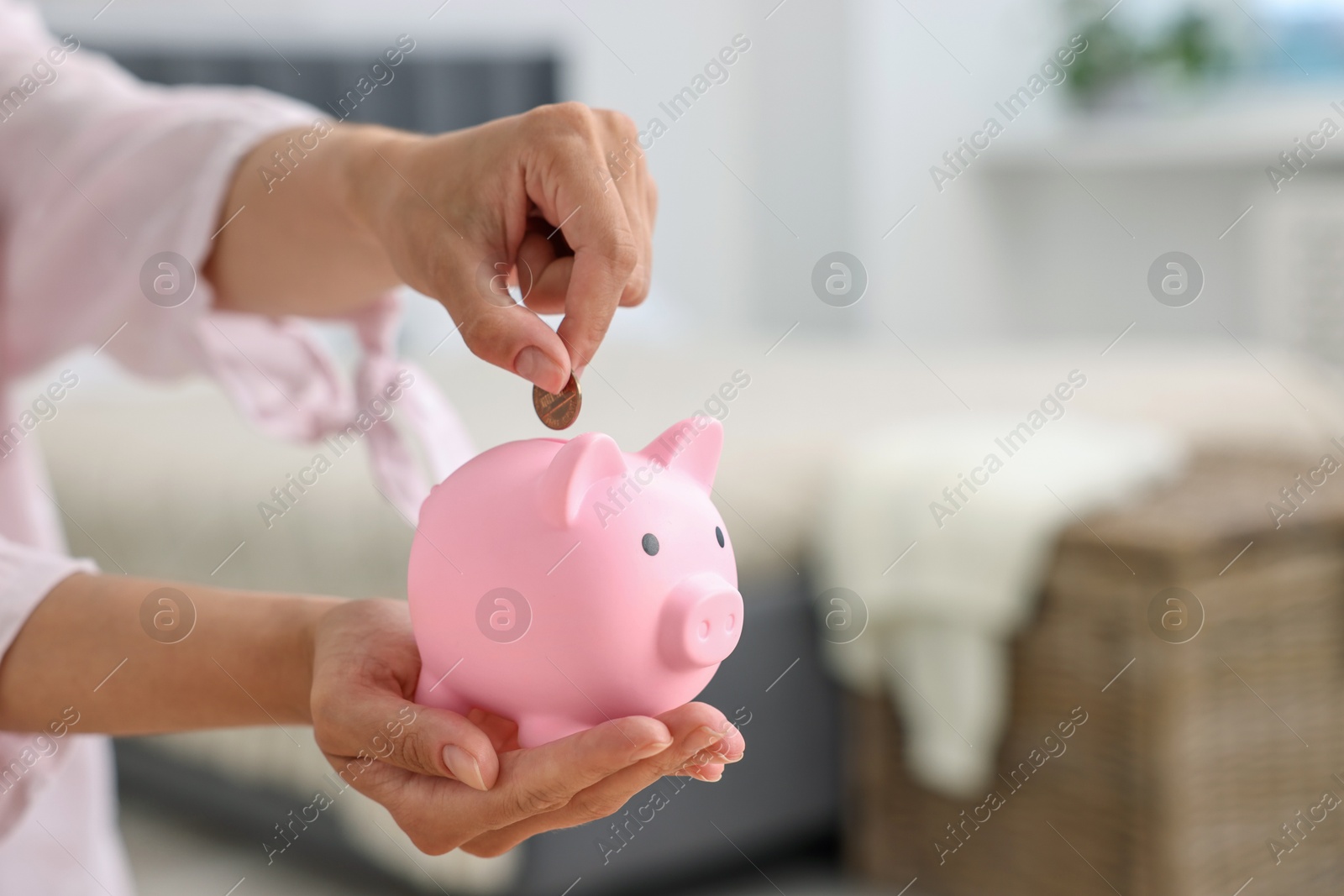 Photo of Woman putting coin into pink piggy bank at home, closeup. Space for text