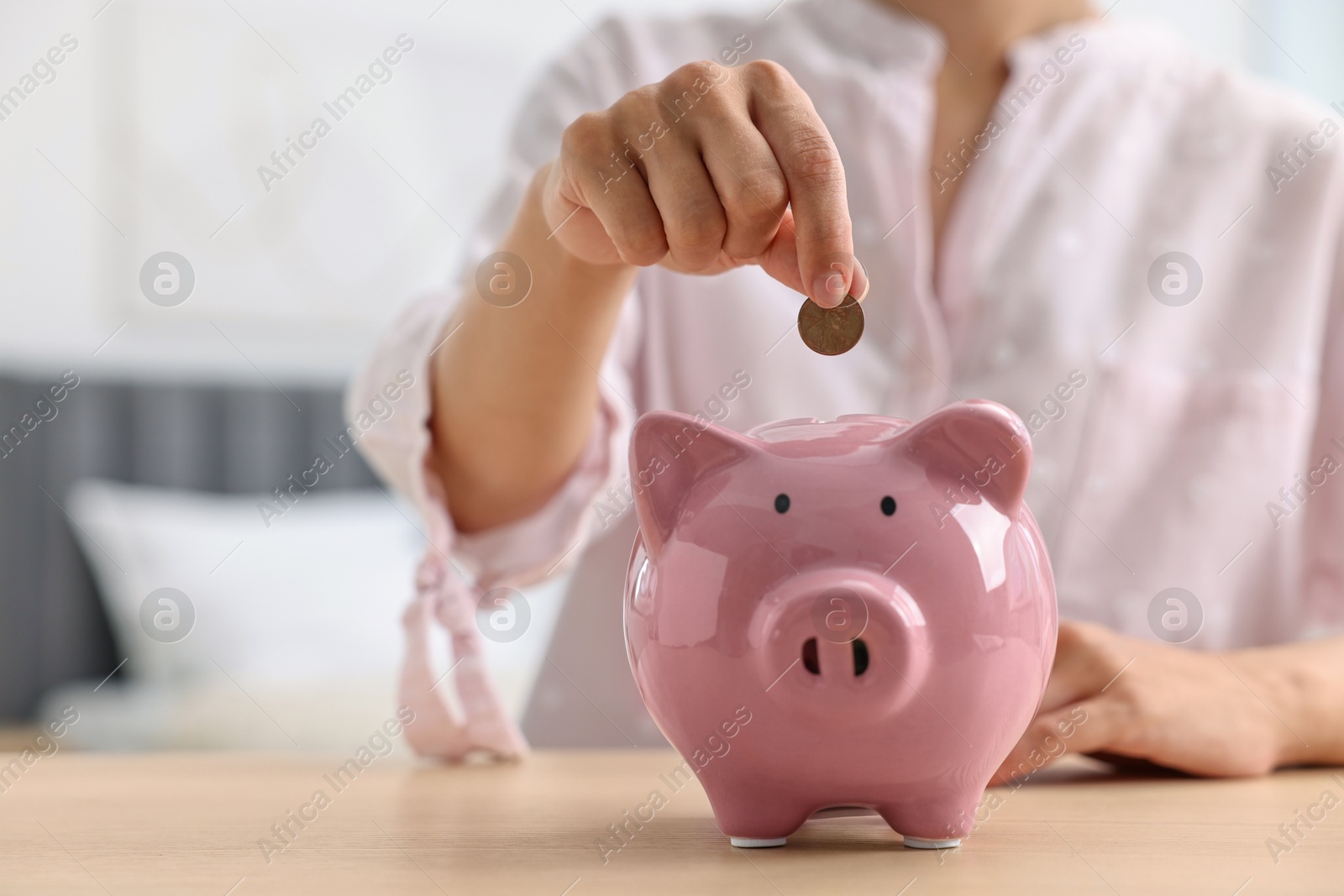 Photo of Woman putting coin into piggy bank at table indoors, closeup. Space for text