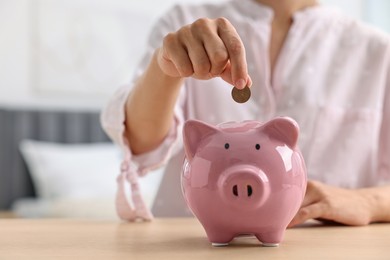 Photo of Woman putting coin into piggy bank at table indoors, closeup. Space for text