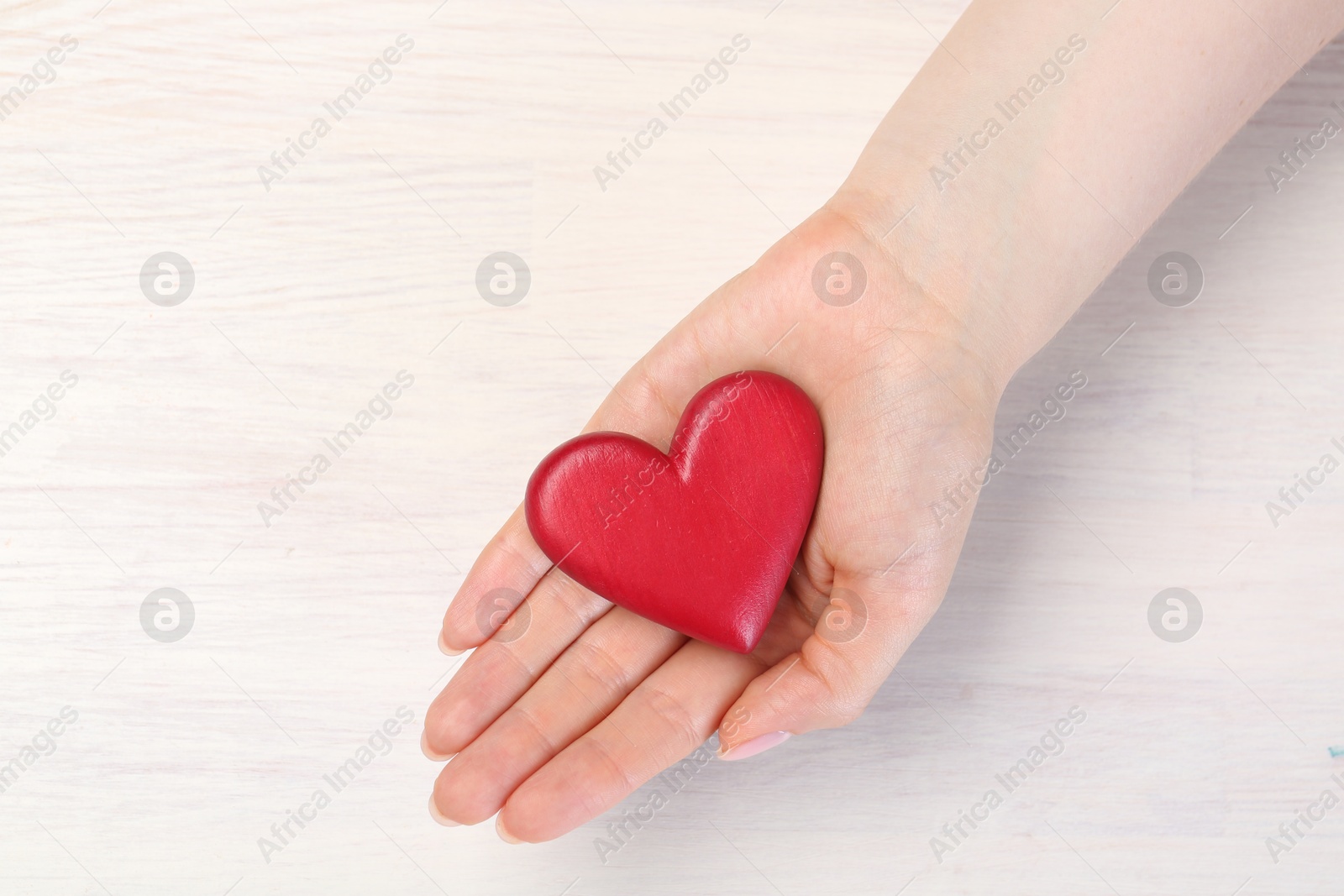 Photo of Woman with red decorative heart at white wooden table, top view. Space for text