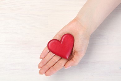 Photo of Woman with red decorative heart at white wooden table, top view. Space for text