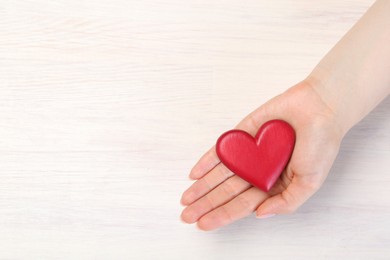 Photo of Woman with red decorative heart at white wooden table, top view. Space for text