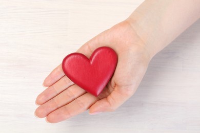 Photo of Woman with red decorative heart at white wooden table, top view