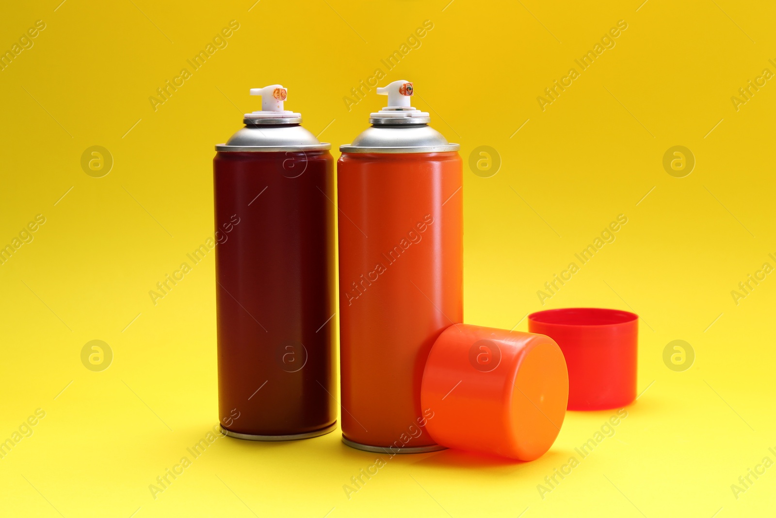 Photo of Two spray paint cans on yellow background