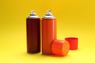 Photo of Two spray paint cans on yellow background