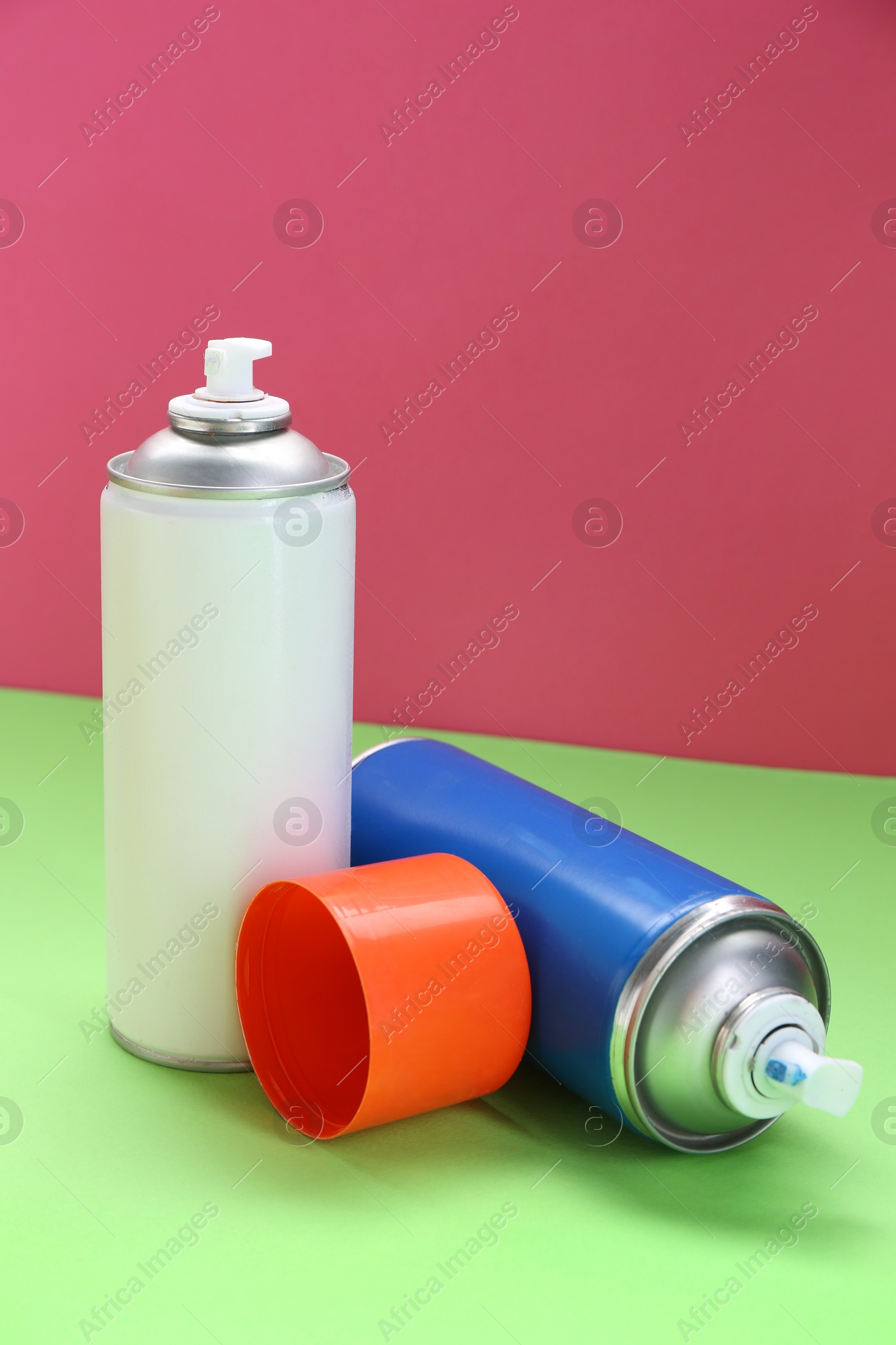 Photo of Two spray paint cans on color background