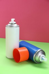 Two spray paint cans on color background