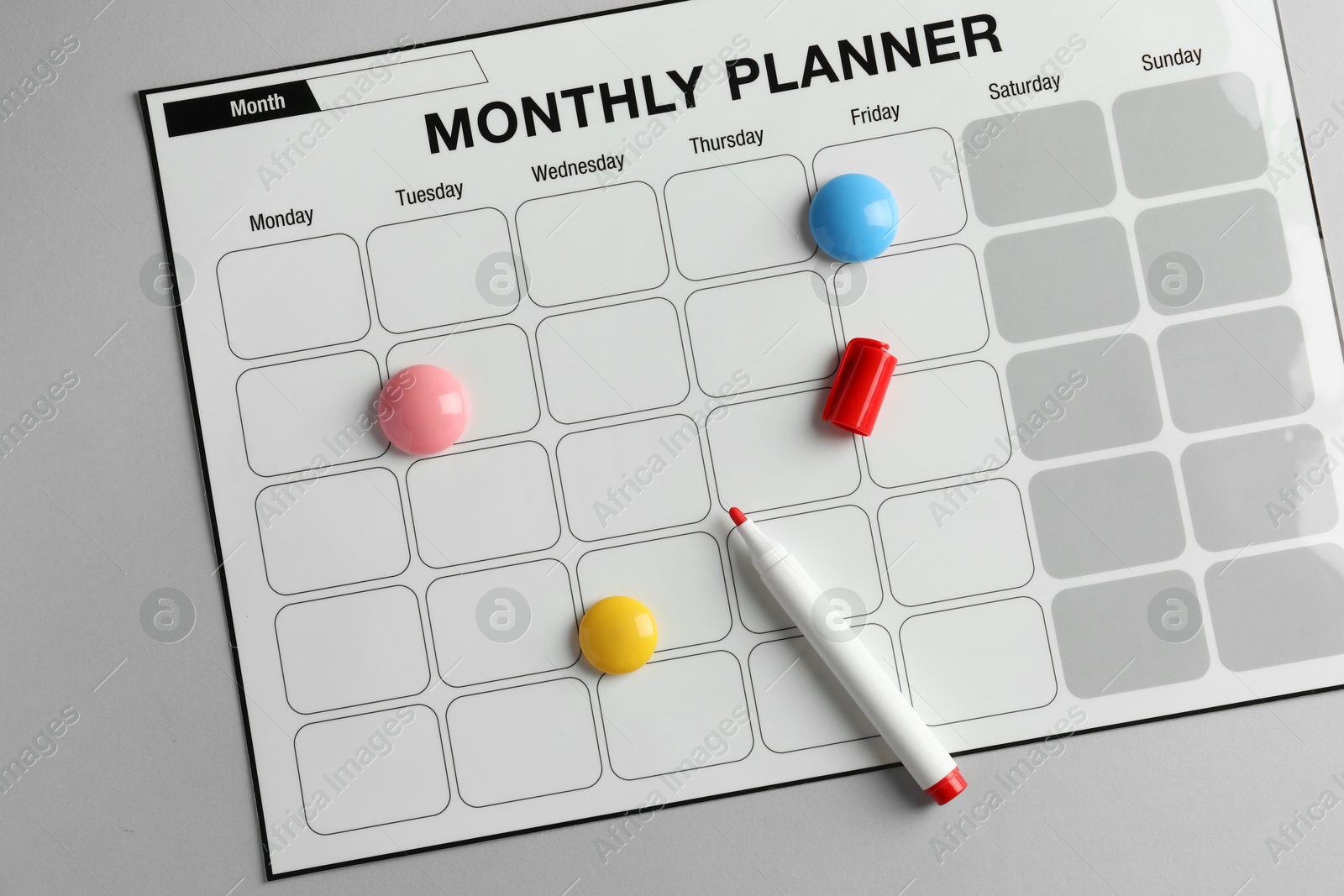 Photo of Timetable. Planner with bright magnets and red felt pen on grey table, top view