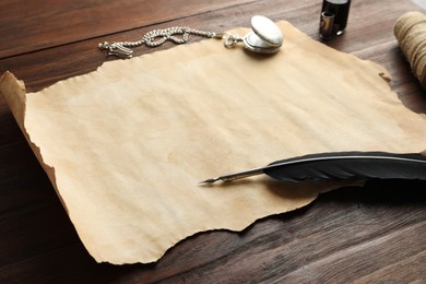 Sheet of old parchment paper, black feather, inkwell and pocket chain clock on wooden table, closeup