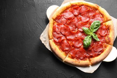 Photo of Tasty pepperoni pizza on black textured table, top view. Space for text