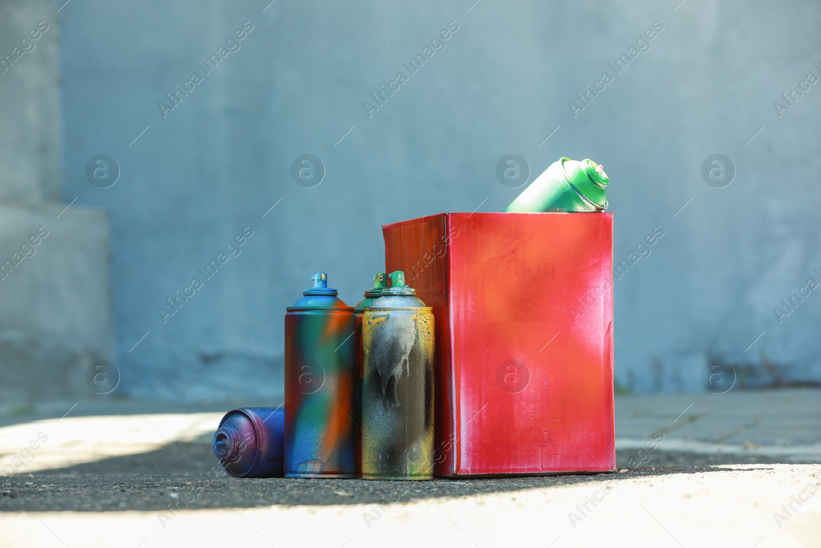 Photo of Many spray paint cans and red cardboard box outdoors