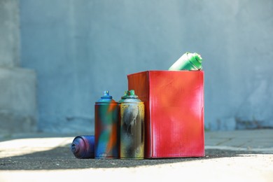 Many spray paint cans and red cardboard box outdoors