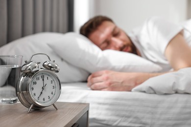 Photo of Handsome young man sleeping in bed at morning, focus on alarm clock