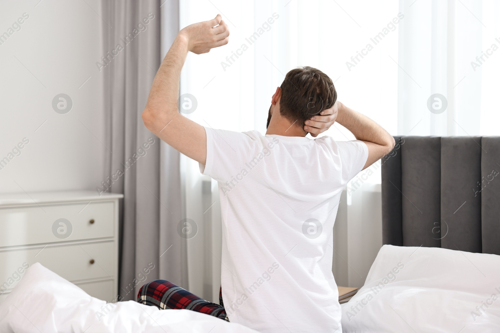 Photo of Young man stretching on bed at morning, back view