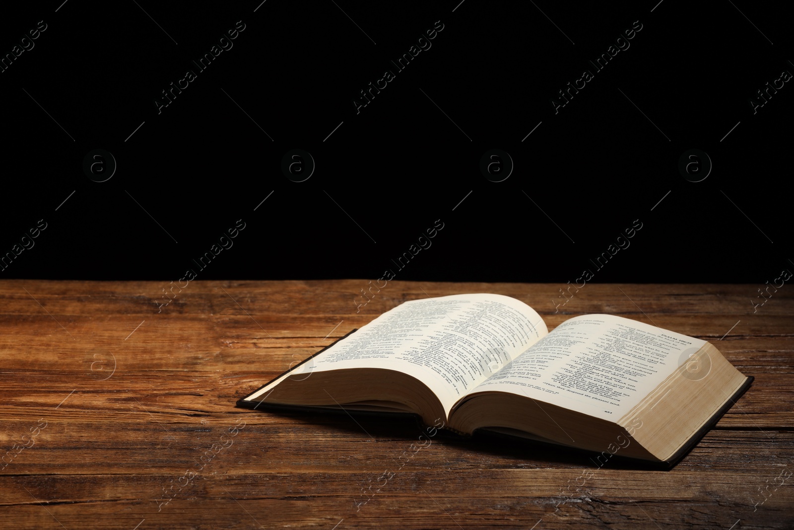 Photo of Bible on wooden table against black background, space for text. Religion of Christianity