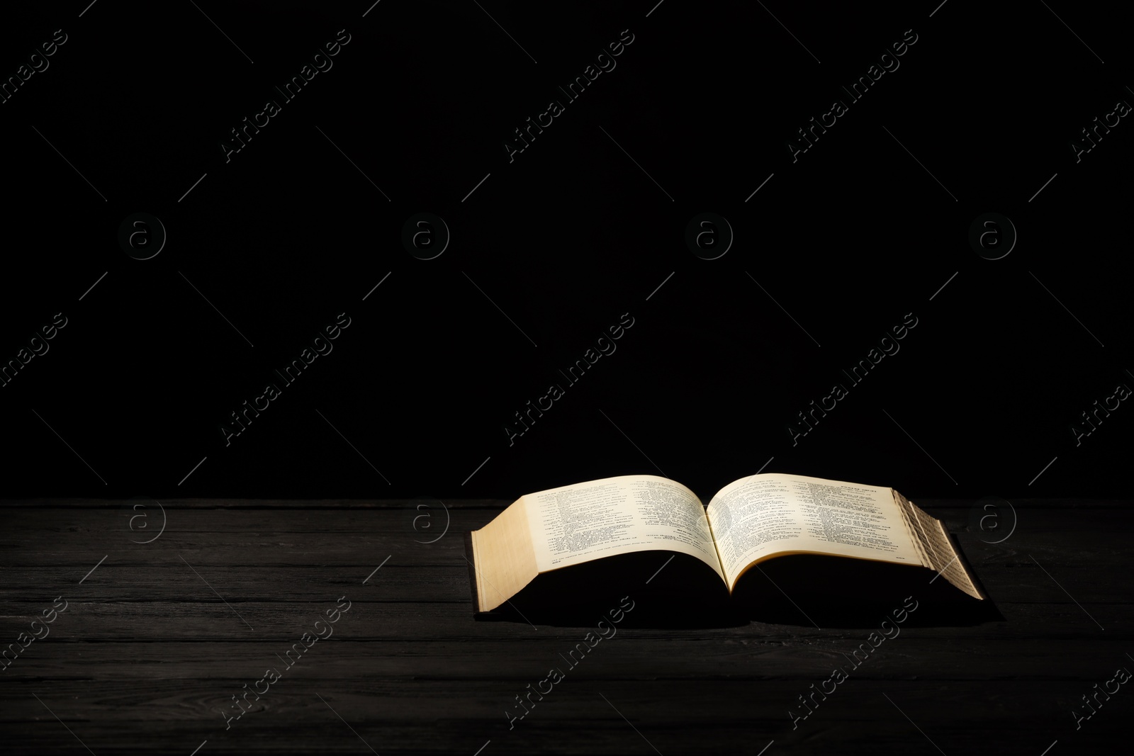 Photo of Bible on dark wooden table against black background, space for text. Religion of Christianity