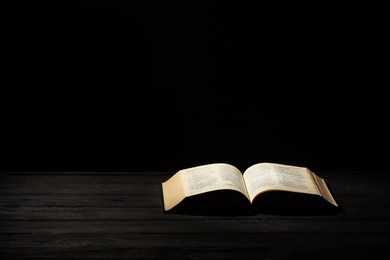 Bible on dark wooden table against black background, space for text. Religion of Christianity