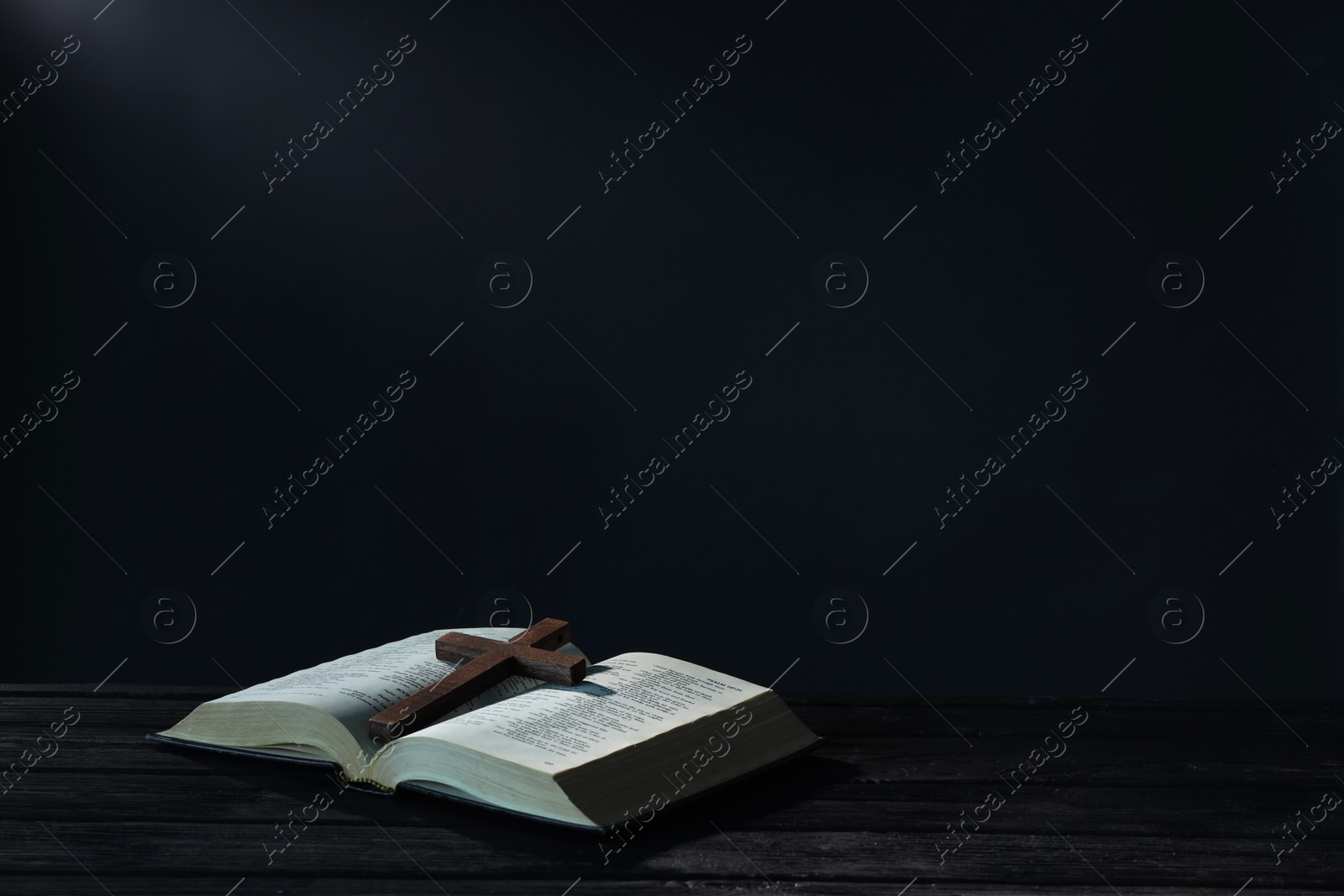 Photo of Bible and cross on black wooden table against dark background, space for text. Religion of Christianity