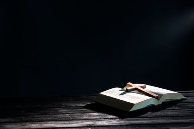 Bible and cross on black wooden table against dark background, space for text. Religion of Christianity