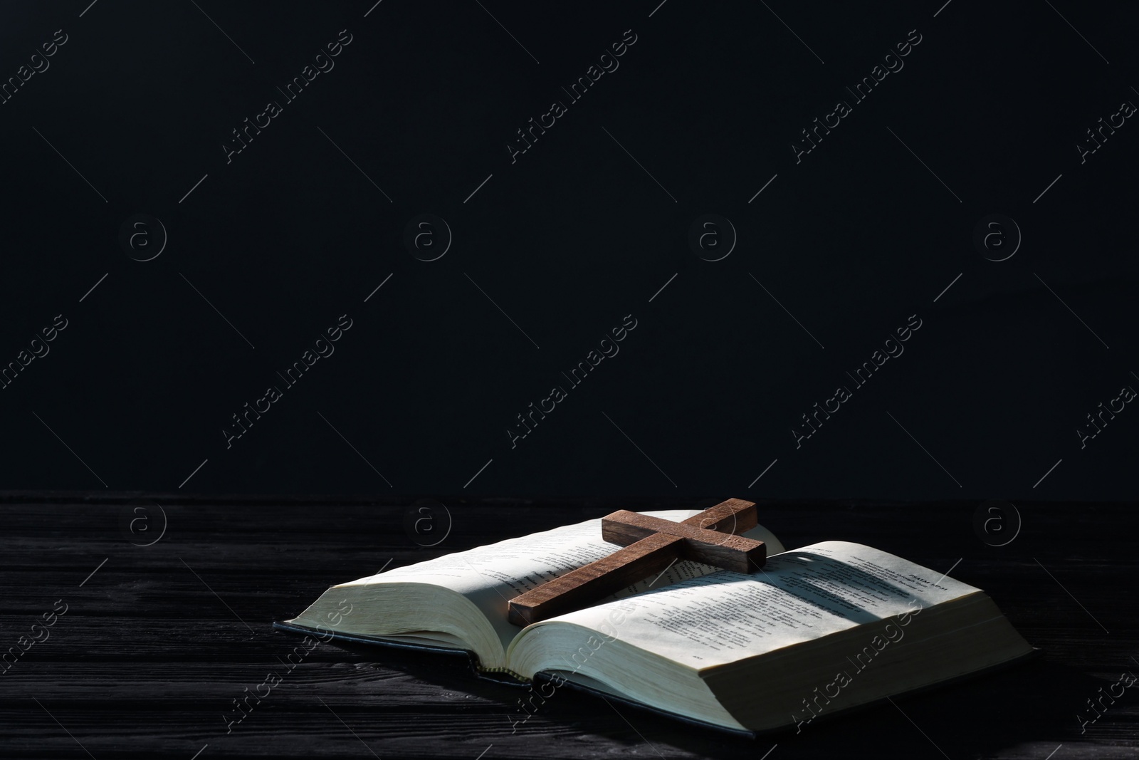 Photo of Bible and cross on black wooden table against dark background, space for text. Religion of Christianity