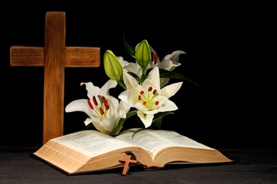 Bible, crosses and lilies on dark gray wooden table against black background. Religion of Christianity