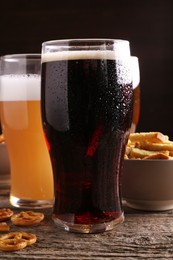 Glasses of beer, pretzel crackers and rusks on wooden table, closeup