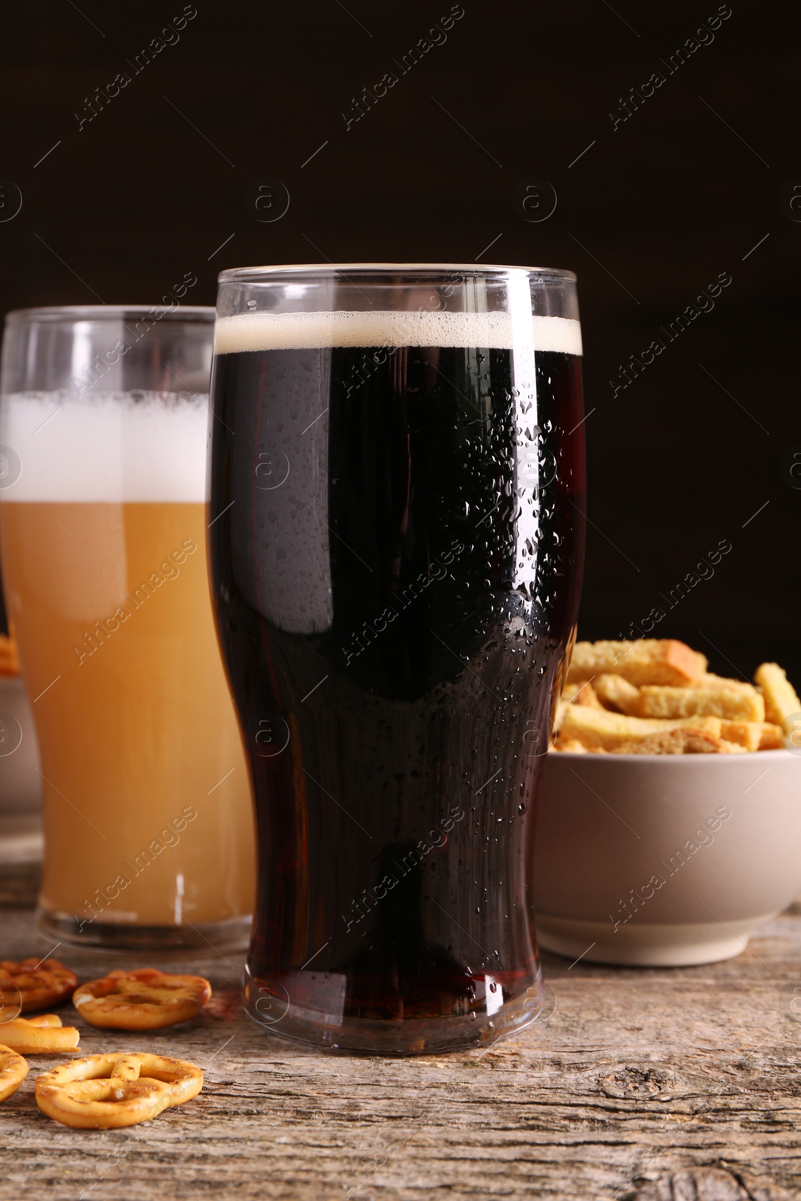 Photo of Glasses of beer, pretzel crackers and rusks on wooden table, closeup