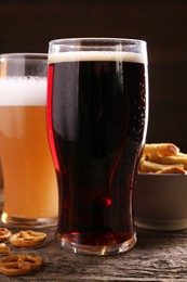 Photo of Glasses of beer, pretzel crackers and rusks on wooden table, closeup