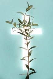 Shining cross and eucalyptus branch on turquoise background. Religion of Christianity