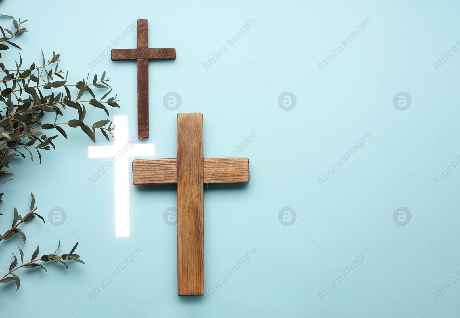 Photo of Many different crosses and eucalyptus branches on light blue background, flat lay with space for text. Religion of Christianity