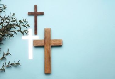 Photo of Many different crosses and eucalyptus branches on light blue background, flat lay with space for text. Religion of Christianity