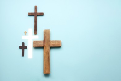 Photo of Many different crosses on light blue background, flat lay with space for text. Religion of Christianity