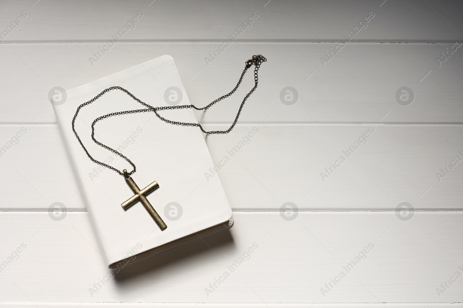 Photo of Cross with chain and Bible on white wooden table, top view with space for text. Religion of Christianity