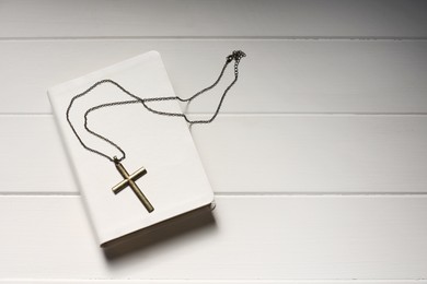 Cross with chain and Bible on white wooden table, top view with space for text. Religion of Christianity