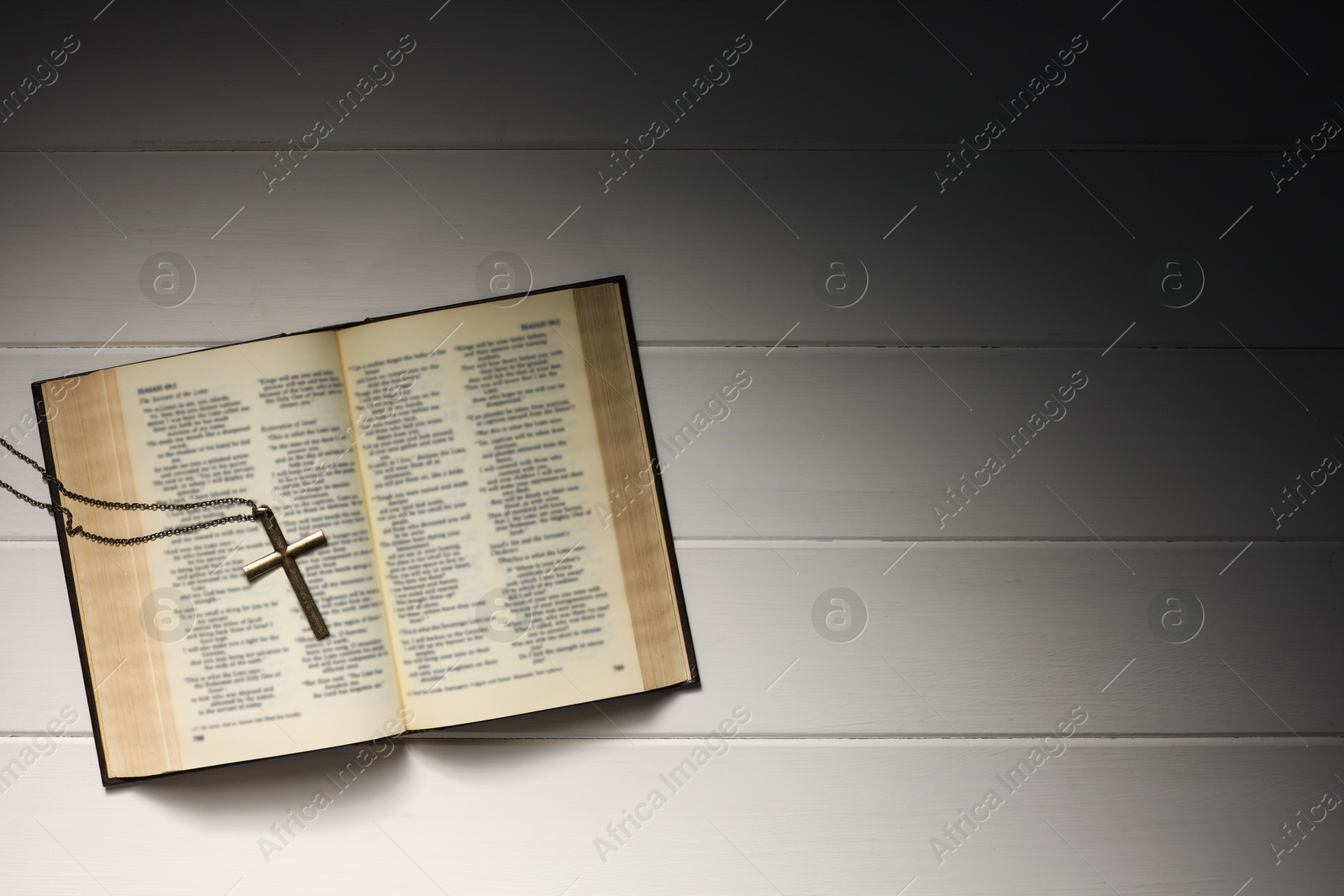 Photo of Cross with chain and Bible on white wooden table, top view with space for text. Religion of Christianity