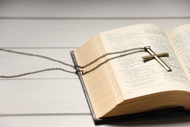 Photo of Cross with chain and Bible on white wooden table, closeup. Religion of Christianity