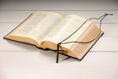 Photo of Cross with chain and Bible on white wooden table, closeup. Religion of Christianity