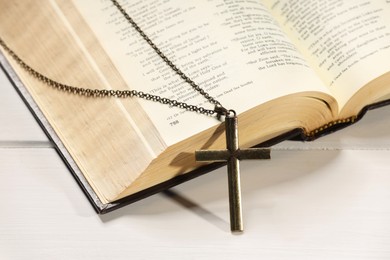 Cross with chain and Bible on white wooden table, closeup. Religion of Christianity