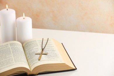 Photo of Cross with chain, burning candles and Bible on white table, closeup with space for text. Religion of Christianity