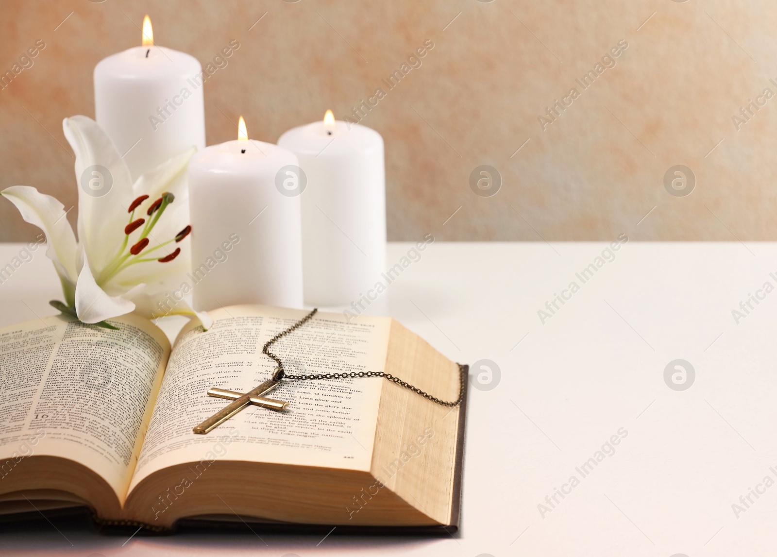 Photo of Cross with chain, burning candles, flower and Bible on white table, closeup with space for text. Religion of Christianity