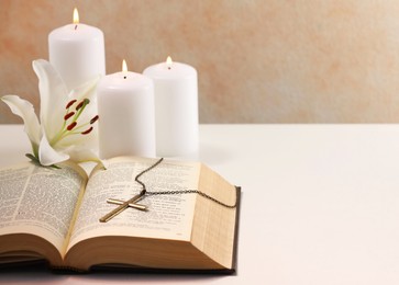 Photo of Cross with chain, burning candles, flower and Bible on white table, closeup with space for text. Religion of Christianity