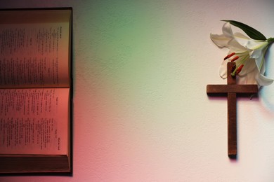 Photo of Wooden cross, Bible and lily flower on textured table in color lights, flat lay with space for text. Religion of Christianity