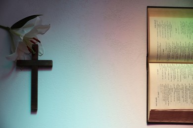 Photo of Wooden cross, Bible and lily flower on textured table in color lights, flat lay with space for text. Religion of Christianity